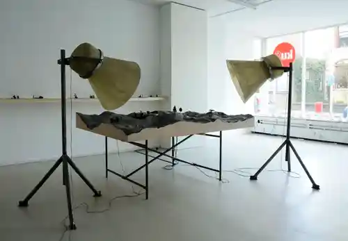 Art installation of a turntable surrounded by miniature figurines and large cone-shaped speakers in a gallery setting.