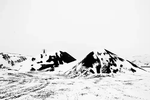 Snow-covered coal-like hills in eastern Iceland, showcasing a black-and-white lithograph-like winter landscape.