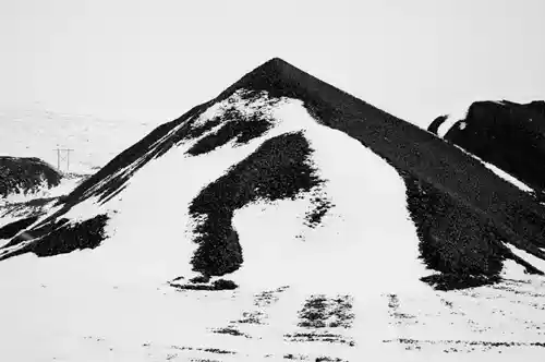 A conical hill of coal-like stone covered in snow, part of the stark Icelandic winter landscape.