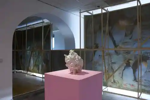 Interior view of an art exhibition with a sculpture on a pink pedestal and screens with animal-themed designs.