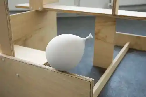 A solid plaster balloon resting on a wooden frame, representing a juxtaposition of weight and form.