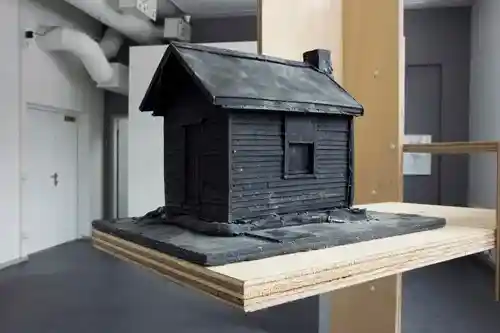 A miniature black wooden cabin model displayed on a layered wooden platform.