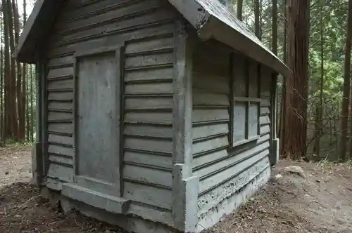 Rustic wooden cabin in a forest, painted in muted tones, surrounded by tall trees.