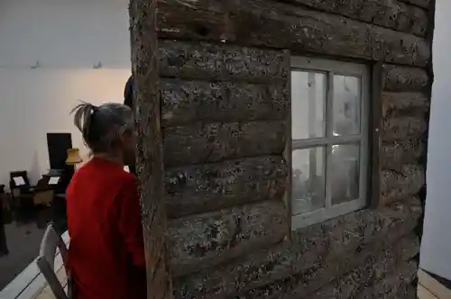 Close-up side view of a rustic wooden cabin wall with a window, placed in an art gallery.